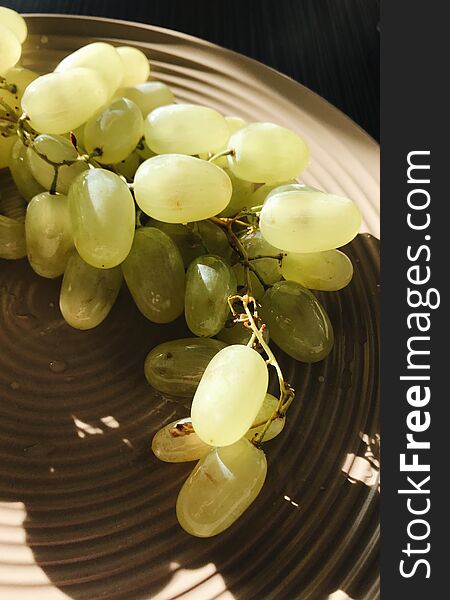 Bunch of white grapes on a plate lit by the sun. Bunch of white grapes on a plate lit by the sun.