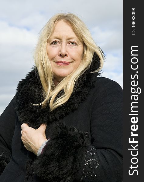 Color portrait photo of a beautiful blonde older lady in her sixties wearing a black winter coat and looking straight at camera. Color portrait photo of a beautiful blonde older lady in her sixties wearing a black winter coat and looking straight at camera.