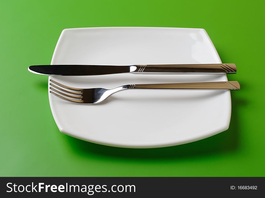 White square plate, knife, and fork on green background