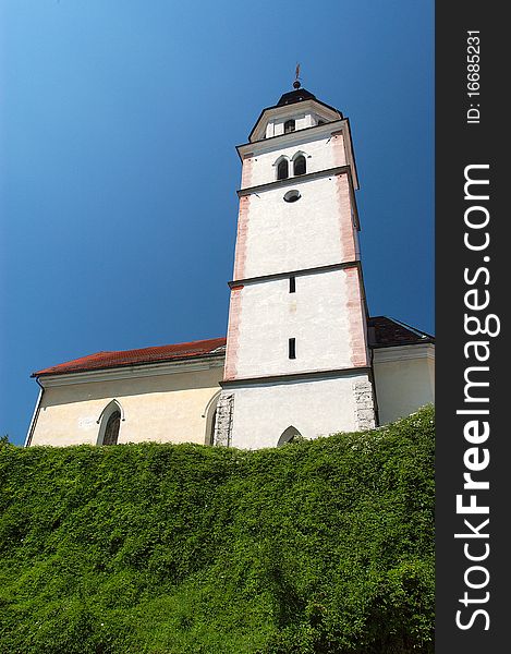 White/yellow church against blue sky with green hedge in front. White/yellow church against blue sky with green hedge in front