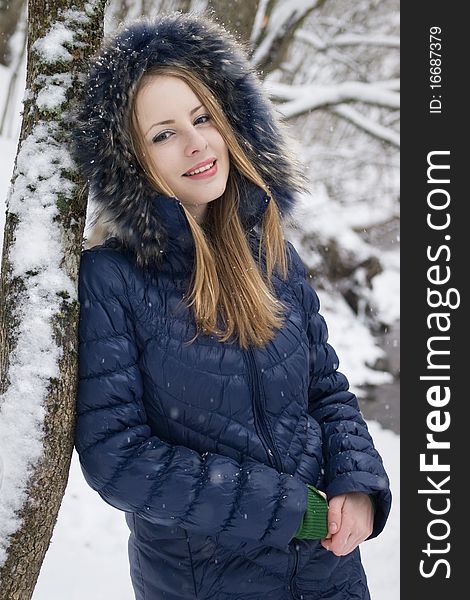 Smiling young woman in blue coat outdoors in snow garden. Smiling young woman in blue coat outdoors in snow garden