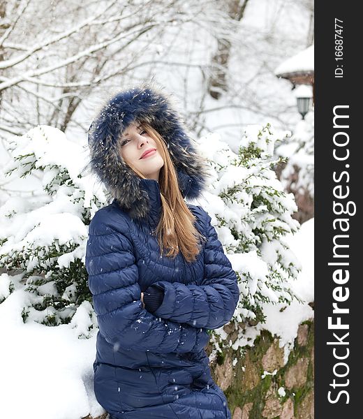 Smiling young woman in blue coat outdoors in snow garden. Smiling young woman in blue coat outdoors in snow garden