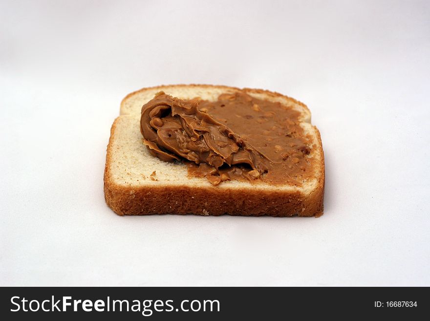A piece of white bread with peanut butter being spread over it. A piece of white bread with peanut butter being spread over it.