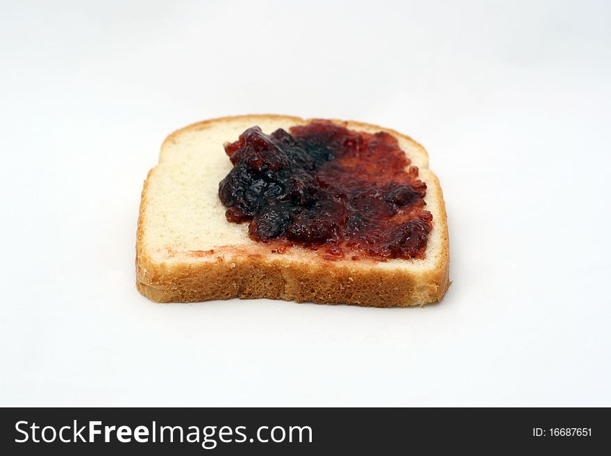 A piece of white bread with strawberry jelly being spread over it. A piece of white bread with strawberry jelly being spread over it.