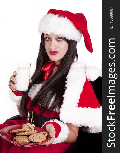 A woman dressed in a santa suit  sitting and enjoying some cookies and milk. A woman dressed in a santa suit  sitting and enjoying some cookies and milk.