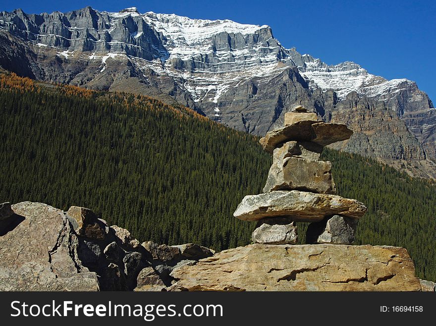 A stone inukshuk or cairn marker with forest and mountains in the background. A stone inukshuk or cairn marker with forest and mountains in the background