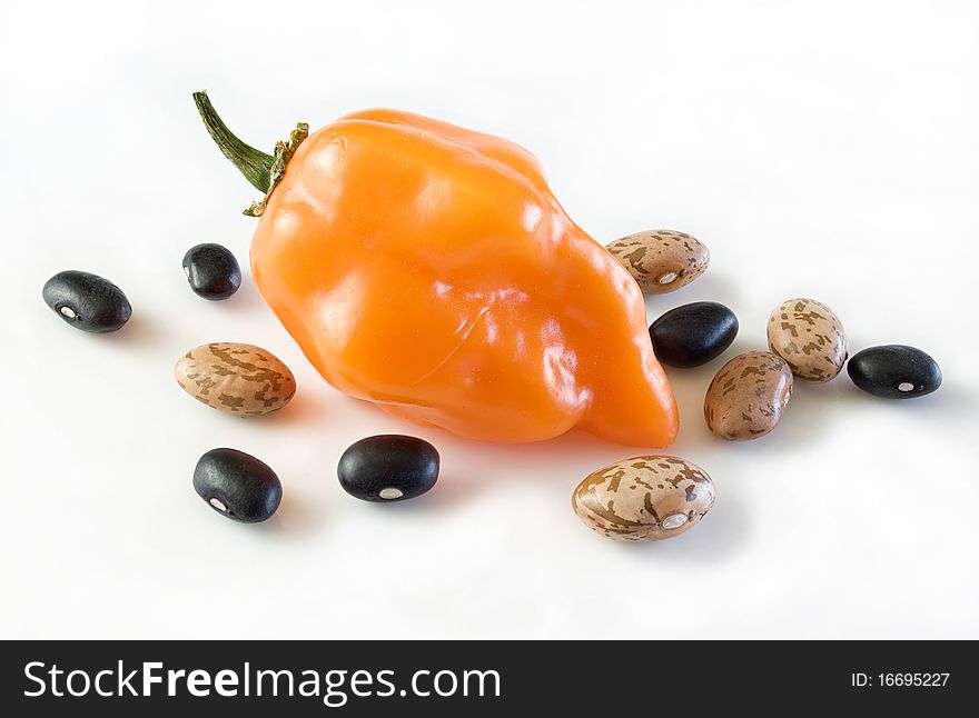 Beautiful ripe golden orange habanero chile surrounded with pinto and black beans, on white. Beautiful ripe golden orange habanero chile surrounded with pinto and black beans, on white.