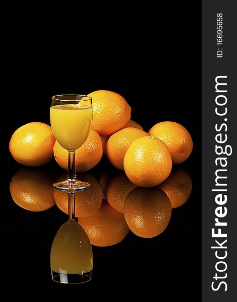 Oranges and glass of fresh orange juice on the black background