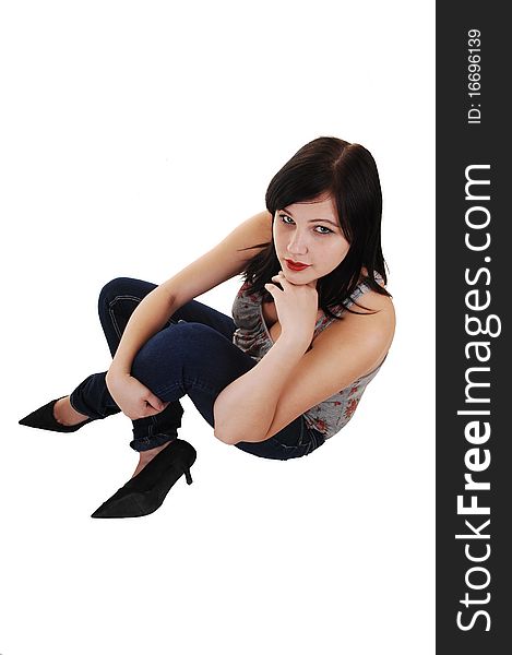 A young pretty woman in jeans and high heels sitting on the floor of a studio, looking up into the camera, on white background. A young pretty woman in jeans and high heels sitting on the floor of a studio, looking up into the camera, on white background.