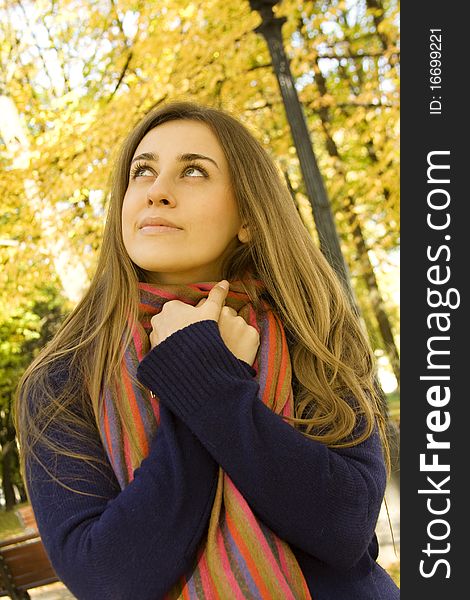 Autumn portrait of a beautiful young woman against yellow leaves. The girl was wrapped in a scarf