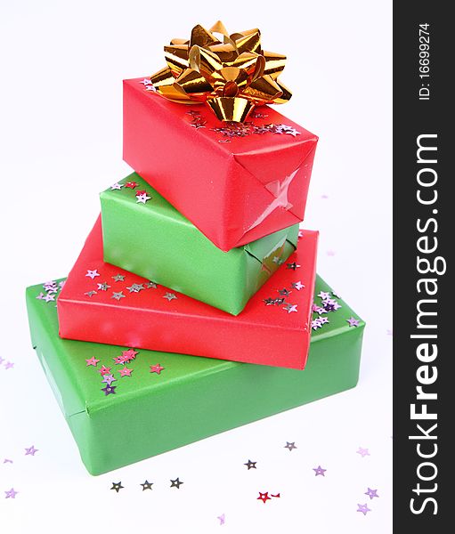 Pile of gifts in green and red wrapping with a golden bow decorated with star shaped confetti