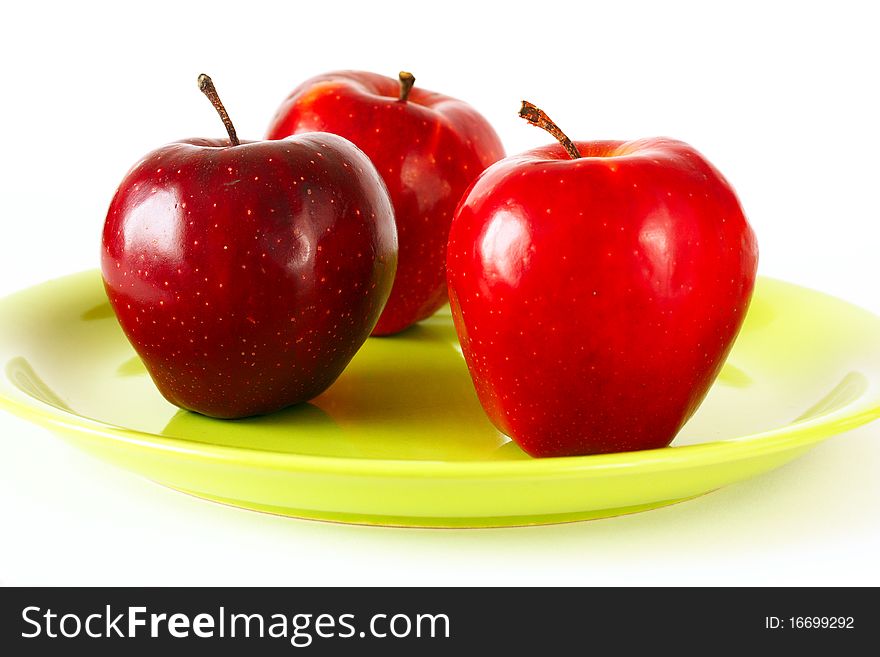 Three Red apples on green plate, white background.