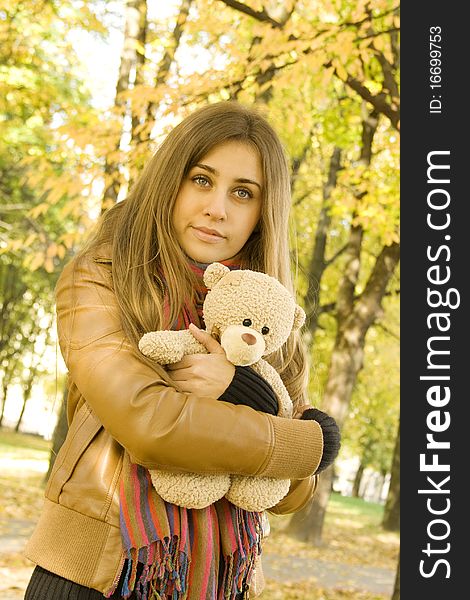 Portrait of a beautiful young woman in autumn park hugging a stuffed toy bear. Portrait of a beautiful young woman in autumn park hugging a stuffed toy bear
