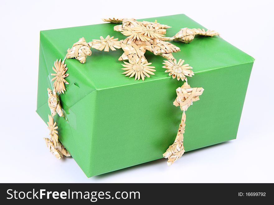 Gift in green wrapping decorated with straw garland on white background