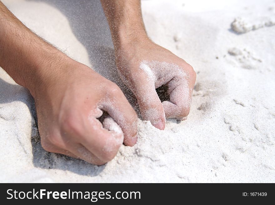 Two hands digging into the sand at a beach while the winds blows