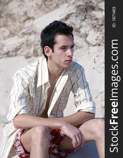 A handsome young man sitting at a beach. A handsome young man sitting at a beach