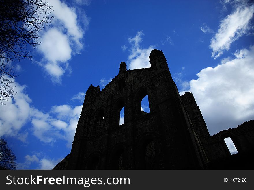 Silhouetted profile of Kirkstall Abbey against a blue sky