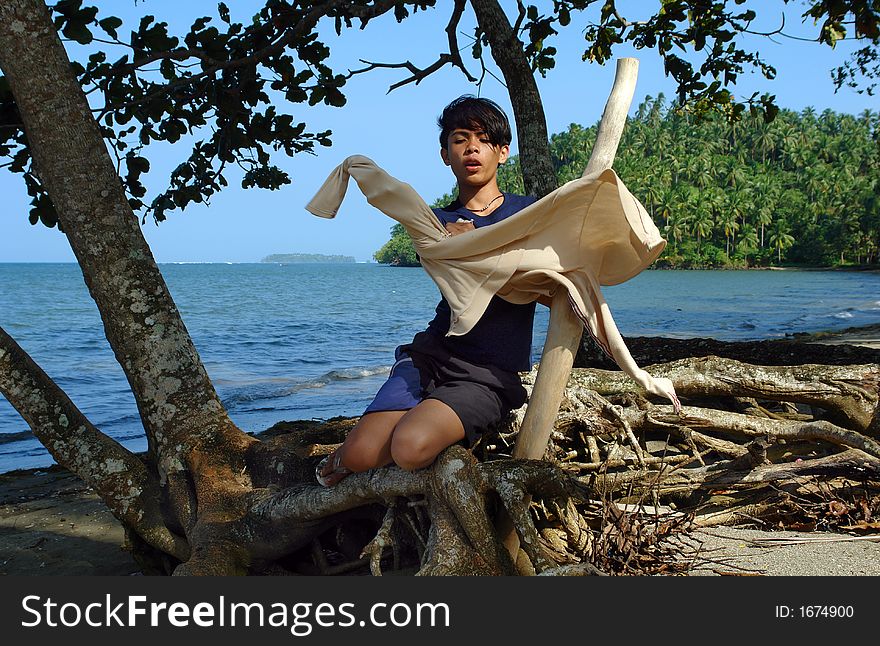 Asian boy pulling a jacket on under the trees near a tropical exotic pristine beach. Asian boy pulling a jacket on under the trees near a tropical exotic pristine beach.