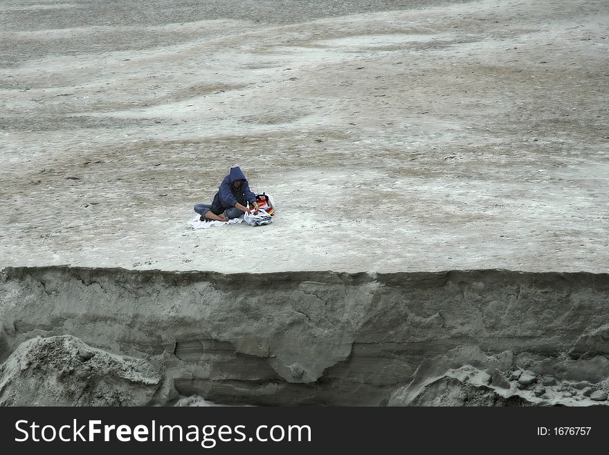 Woman picnicing alone on an empty beach on a chilly, overcast day. Woman picnicing alone on an empty beach on a chilly, overcast day.