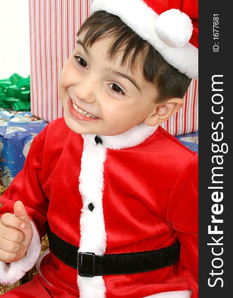 Toddler boy dressed in Santa suit sitting on packages.  Smiling. Toddler boy dressed in Santa suit sitting on packages.  Smiling.