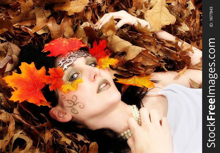 Beautiful young woman with leaves and glitter on face.  Laying in leaves. Wearing white dress. Beautiful young woman with leaves and glitter on face.  Laying in leaves. Wearing white dress.