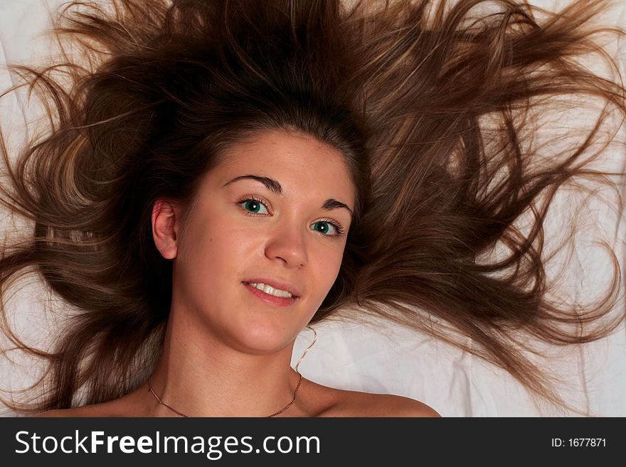 Beautiful girl with green eyes lying on white bedheet