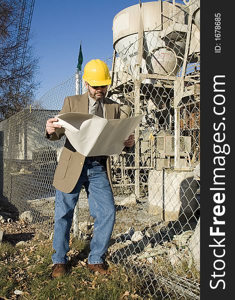 Man in suit at construction site holding bluerints and wearing yellow hardhat. Man in suit at construction site holding bluerints and wearing yellow hardhat.