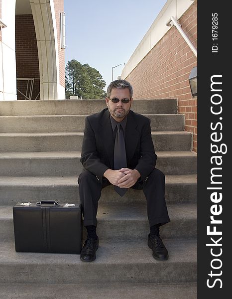 Fourty something business man sitting on steps outside office.  Briefcase and sunglasses. Fourty something business man sitting on steps outside office.  Briefcase and sunglasses.