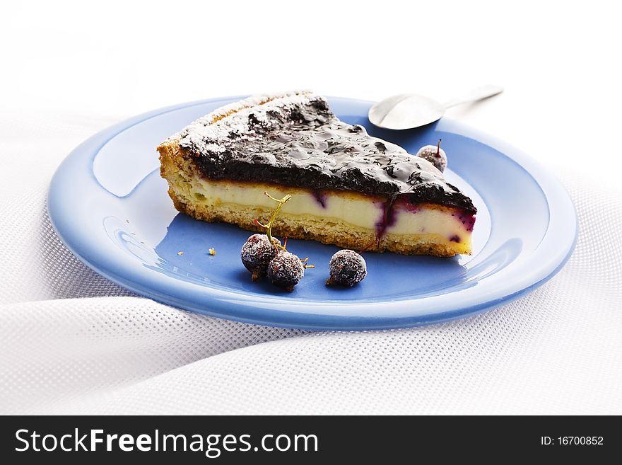 A slice of Blueberries Tart with Black Currant served on a blue platter and on linen tablecloths. A slice of Blueberries Tart with Black Currant served on a blue platter and on linen tablecloths