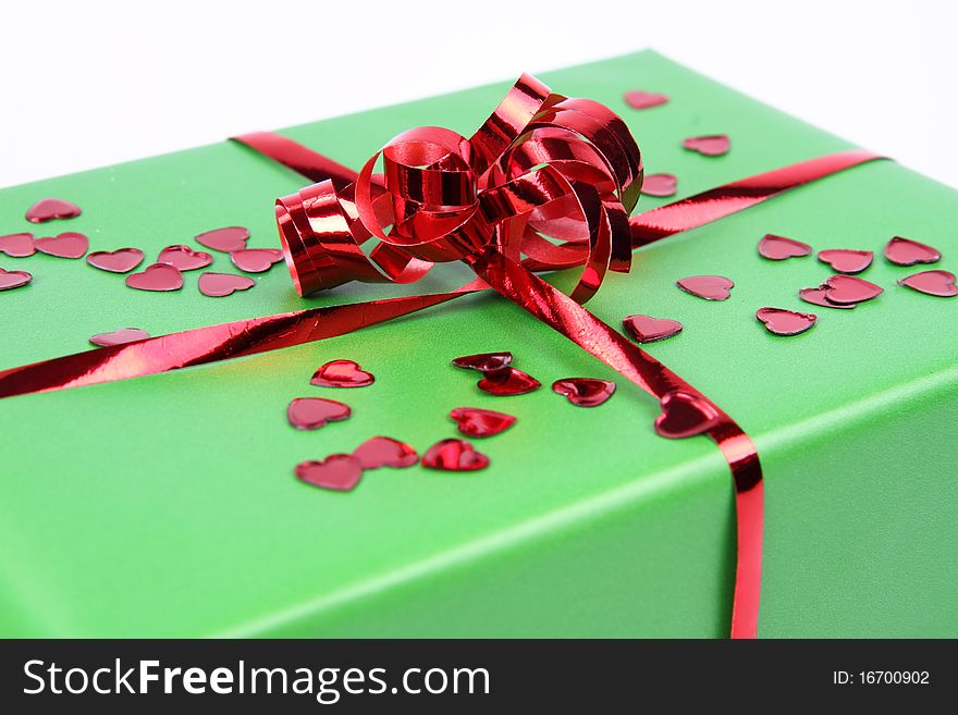 Gift in green wrapping with a red bow decorated with heart shaped confetti in close up. Gift in green wrapping with a red bow decorated with heart shaped confetti in close up