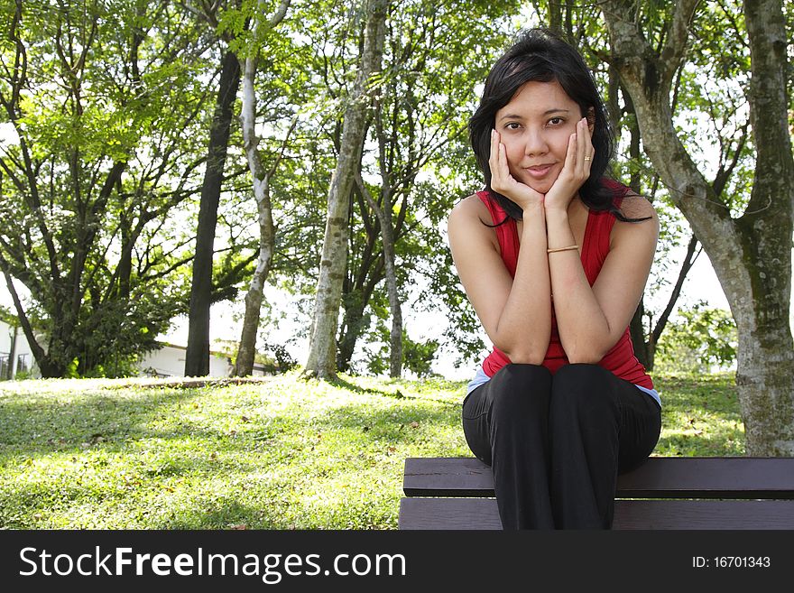 An Asian woman sitting on a bench at a park. An Asian woman sitting on a bench at a park