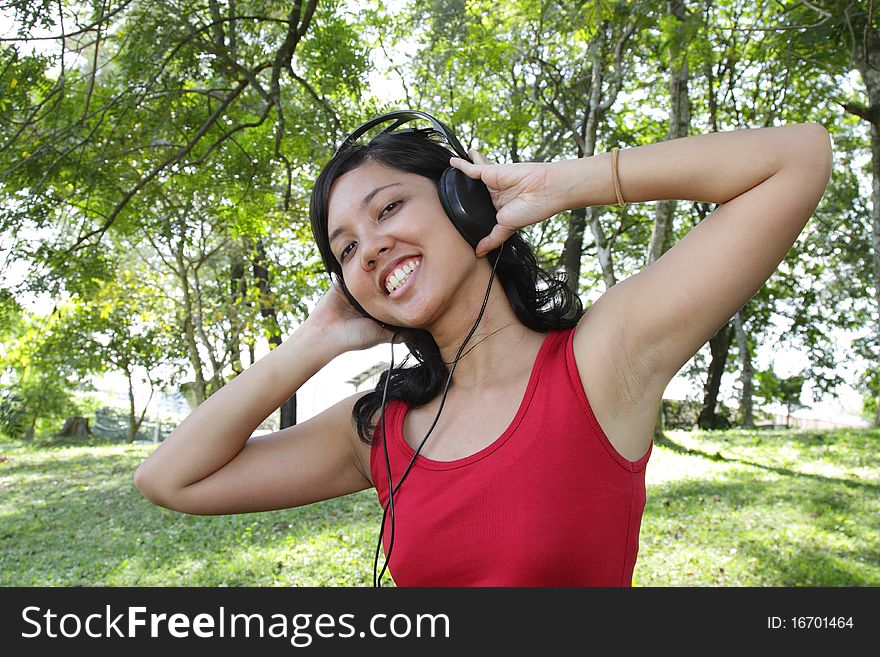 An Asian woman listening to music on headphones at a park