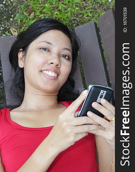 An Asian woman using her hand phone on a bench. An Asian woman using her hand phone on a bench