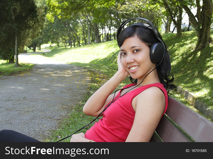 An Asian woman listening to music on headphones at a park