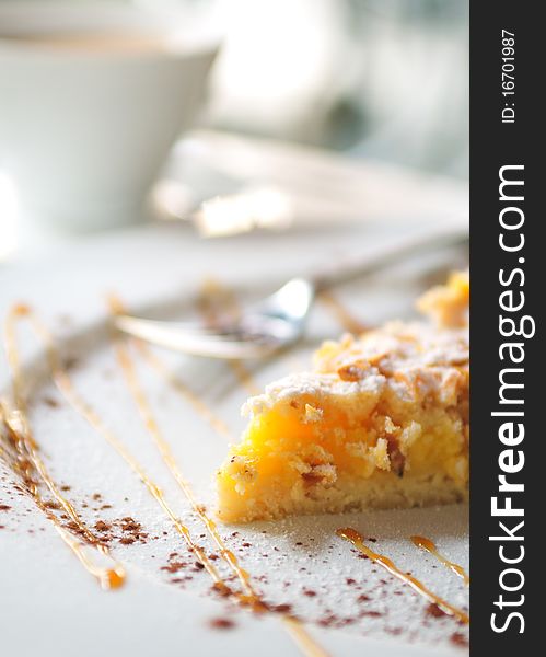 Lemon crusted top tart cake on white plate with a cup of tea in background. Lemon crusted top tart cake on white plate with a cup of tea in background.