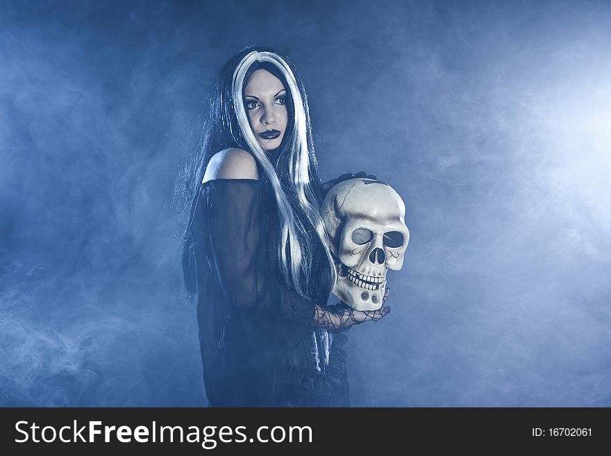 Halloween witch with a skull over black background with white smoke