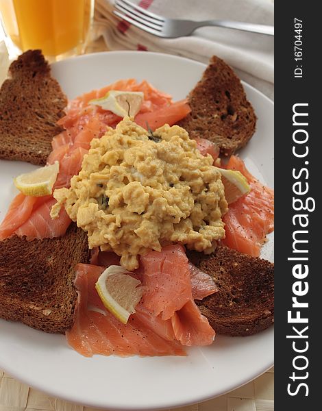 A luxury breakfast of scrambled eggs and smoked salmon served with lemon wedges, wholemeal bread and a glass of orange juice. A luxury breakfast of scrambled eggs and smoked salmon served with lemon wedges, wholemeal bread and a glass of orange juice.