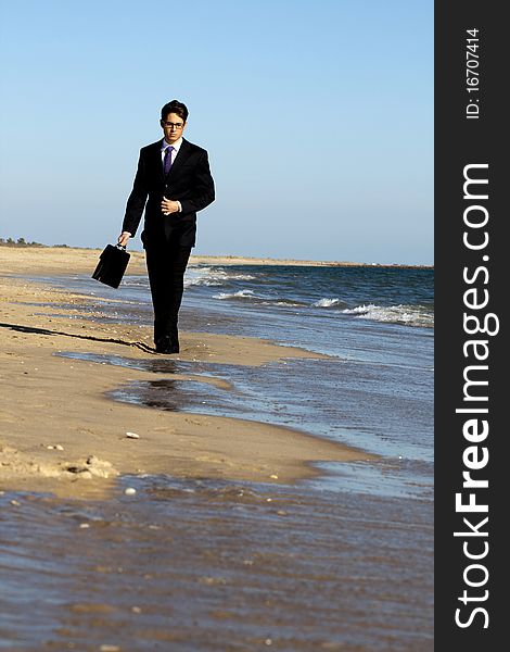 View of a young business man walking down the beach. View of a young business man walking down the beach.