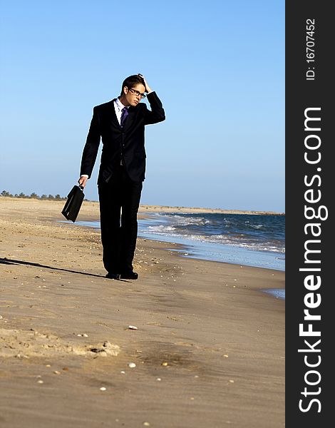 View of a young business man walking down the beach. View of a young business man walking down the beach.