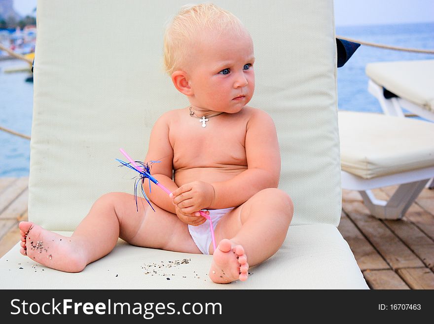 Beautiful baby's sitting with cocktail straw on a beach chair on a pier. Beautiful baby's sitting with cocktail straw on a beach chair on a pier