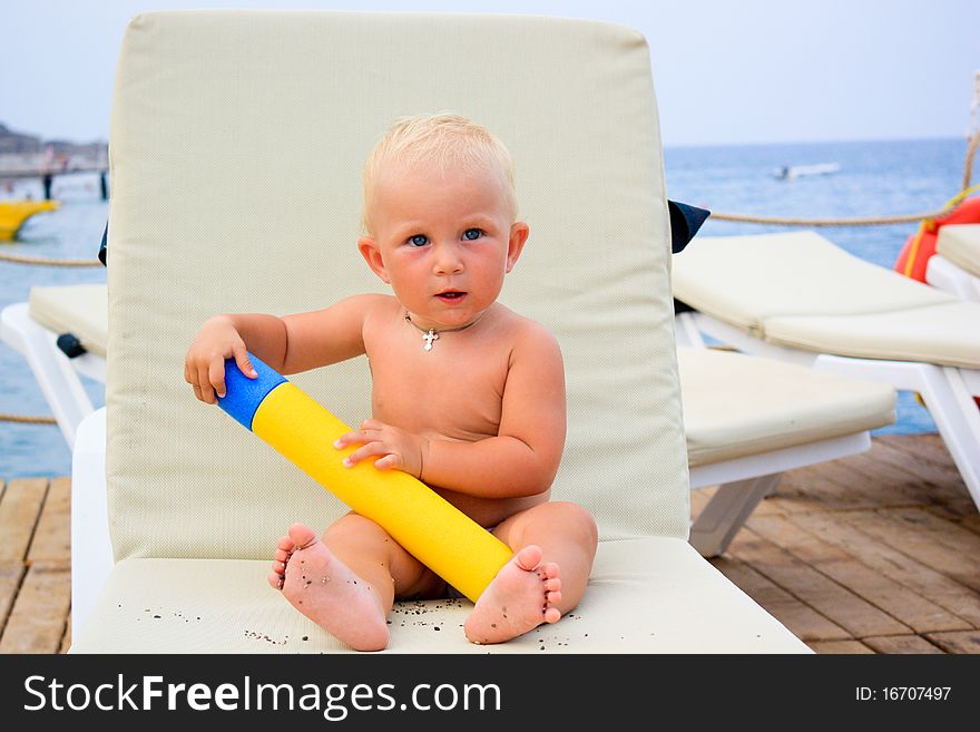 Beautiful baby's sitting with water toy on a beach chair on a pier. Beautiful baby's sitting with water toy on a beach chair on a pier