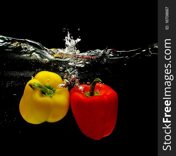 Red and yellow peppers splashing into water over black