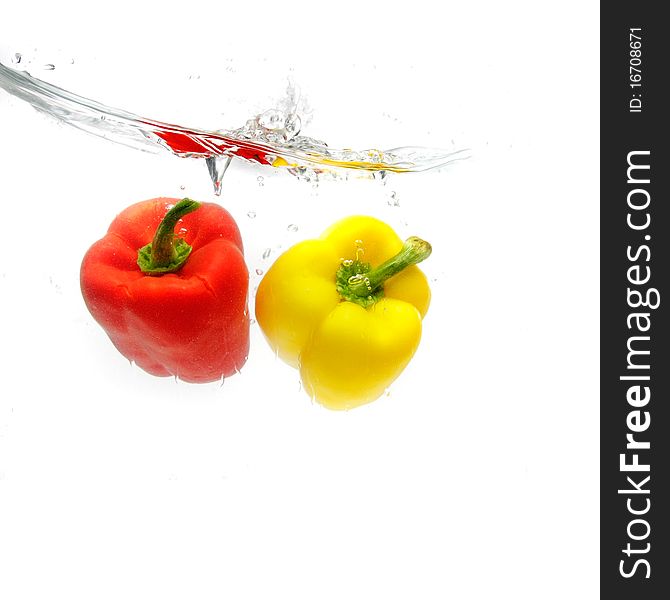 Red and yellow peppers splashing into water over white