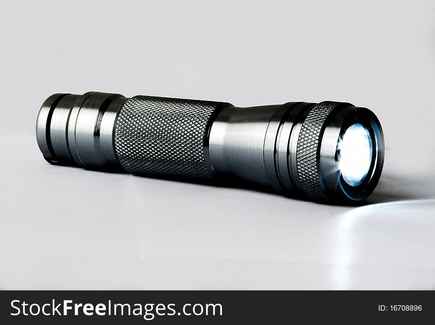 Silver metallic LED flash light on plain background. Flash light is on.