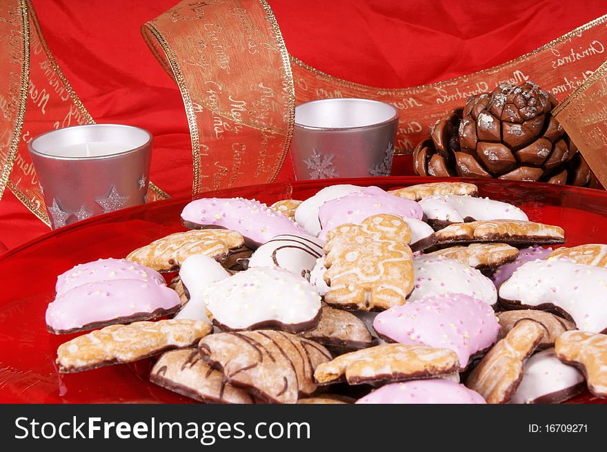 Gingerbread cookies in a red plate with silver candles, pine cones and Christmas ribbon. Studio shot over red background. Shallow DOF. Gingerbread cookies in a red plate with silver candles, pine cones and Christmas ribbon. Studio shot over red background. Shallow DOF.