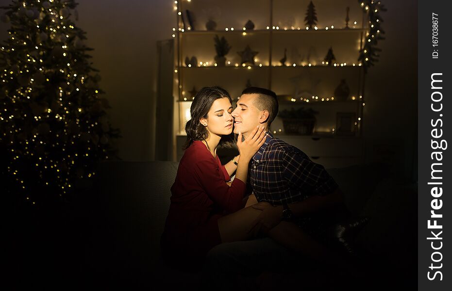 Happy, couple in love in the dark, evening on the couch, dark background, christmas tree lights. Christmas evening. New Year. hug and kiss. attraction, romantic evening and date
