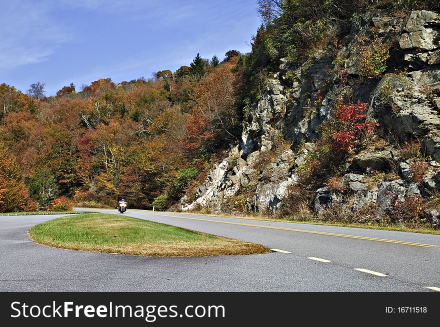 Motorcyclist coming around the curve on a highway in autumn. Motorcyclist coming around the curve on a highway in autumn.