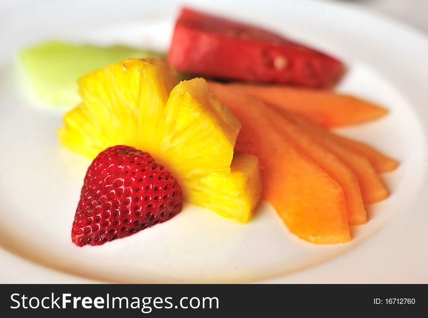 Healthy fruit salad prepared with different colored fruits on white plate.