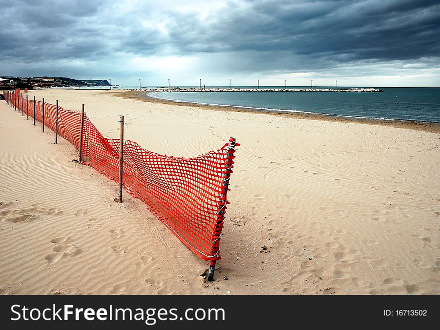 Sandy beach in fall with wind barrier and stormy sky