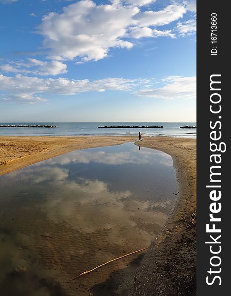 A man walks on deserted beach in early morning of a bright sunny day. A man walks on deserted beach in early morning of a bright sunny day